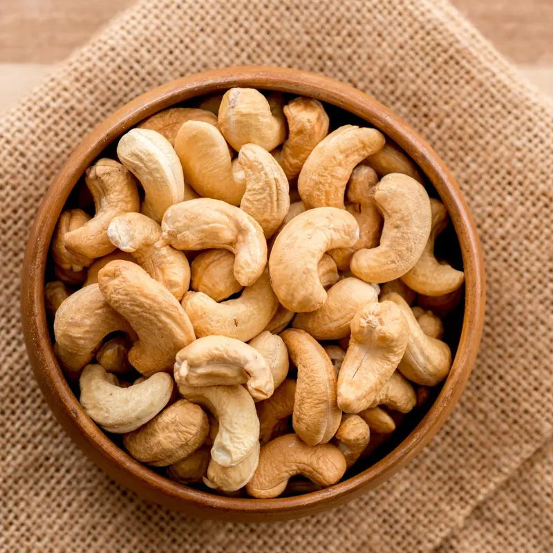 Wooden bowl filled with cashews on a textured brown fabric background